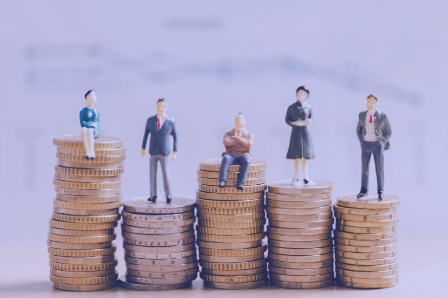 Miniature business figures standing on coin stacks